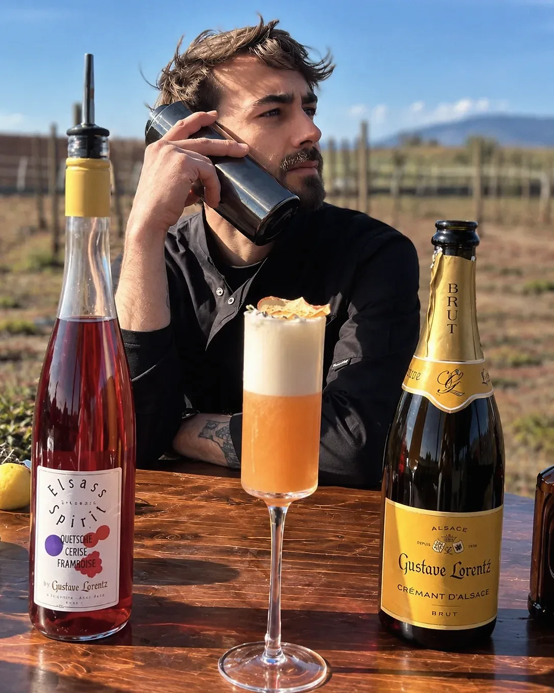 Lukas Guyot, un shaker contre l'oreille comme un téléphone, devant une bouteille Elsass Spirit, une création mousseuse et un crémant Gustave Lorentz, au milieu des vignes.