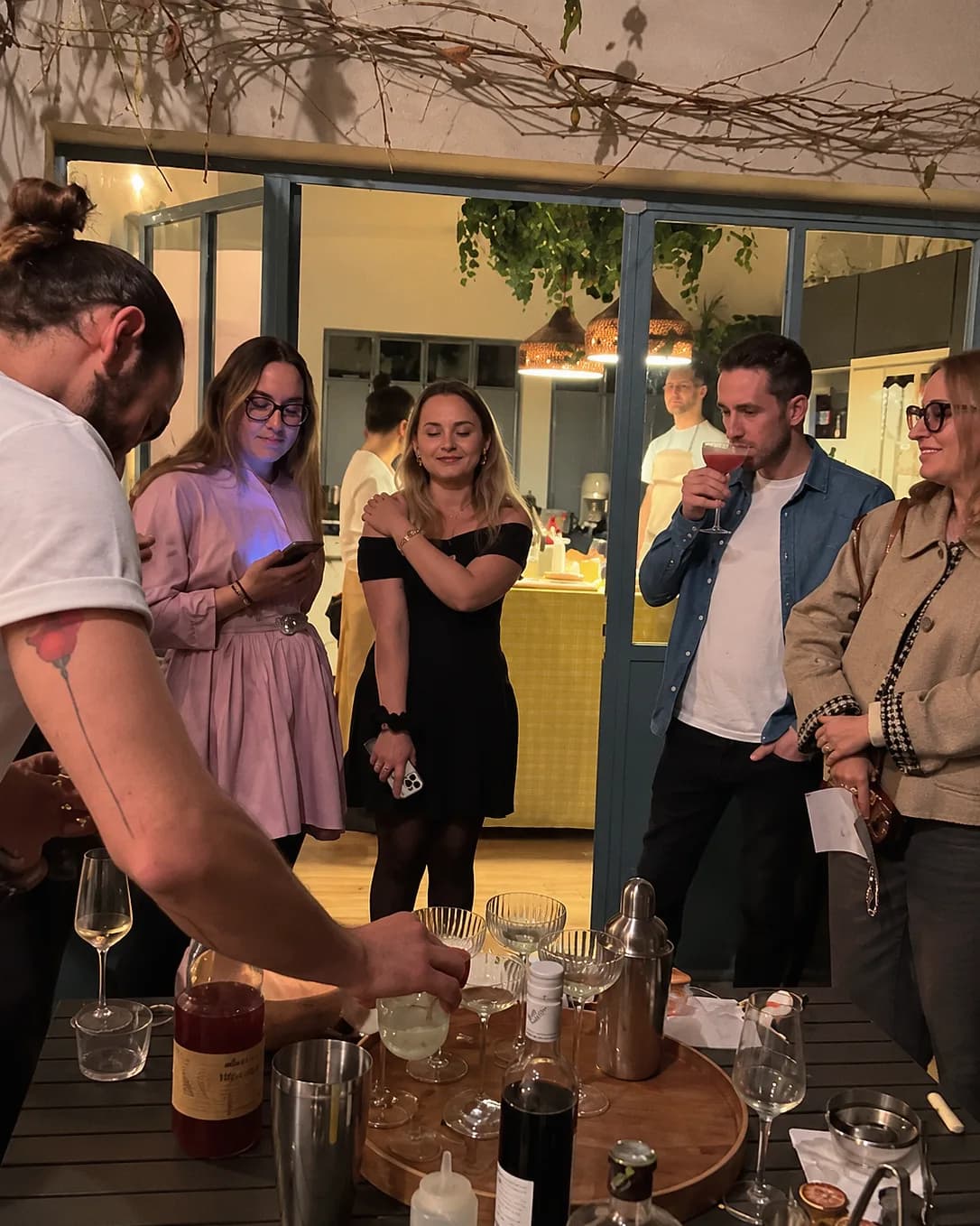 Un groupe de collègues partage un moment convivial autour d’un shaker, en terrasse à la tombée de la nuit.